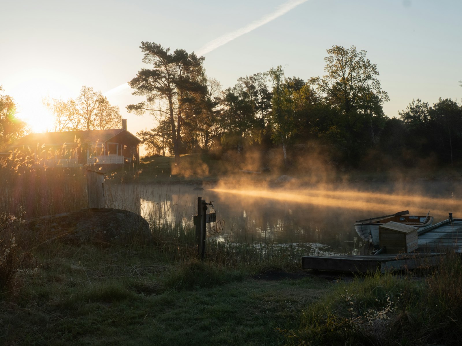 Zonsopgang boven een mistig meer met bomen en een huis aan de oever